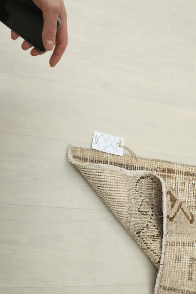Hand holding a tag near the folded rug, indicating its authenticity and quality.