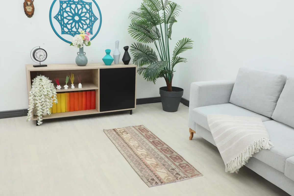 Vintage Anatolian rug placed on a light floor in a room setting with a sofa and cabinet.