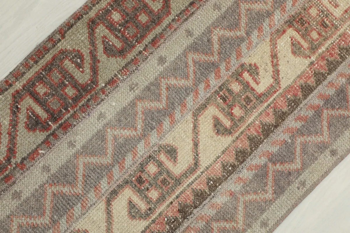 Diagonal close-up view of the rug's patterns, showing the beige, gray, and rust wool pile.