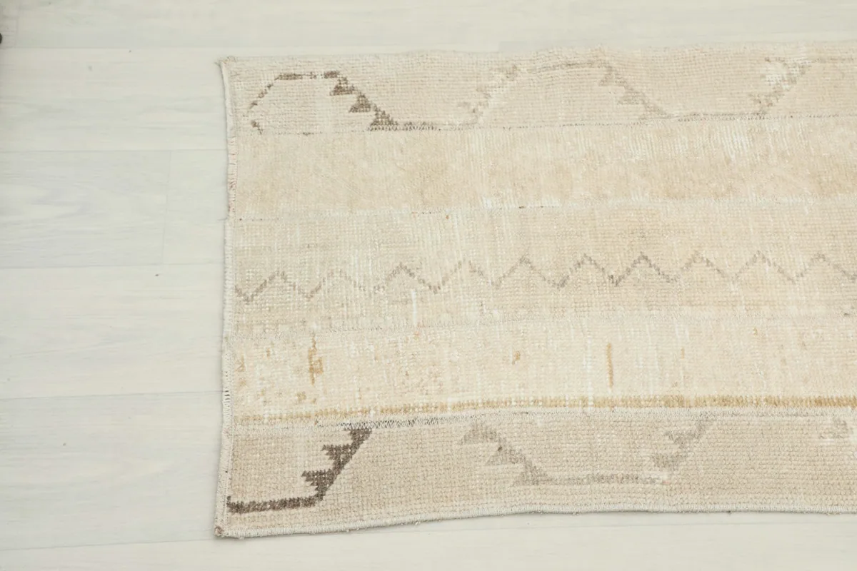 Close-up detail of the other end of the beige runner rug, showing the wool pile and pattern variations.