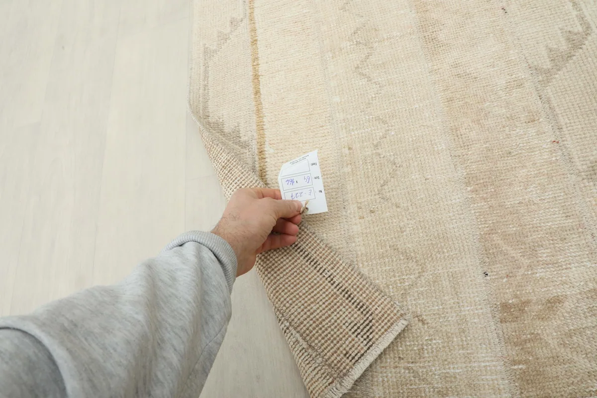 Hand holding a measurement tag near the rug, illustrating the scale and texture of the wool pile.