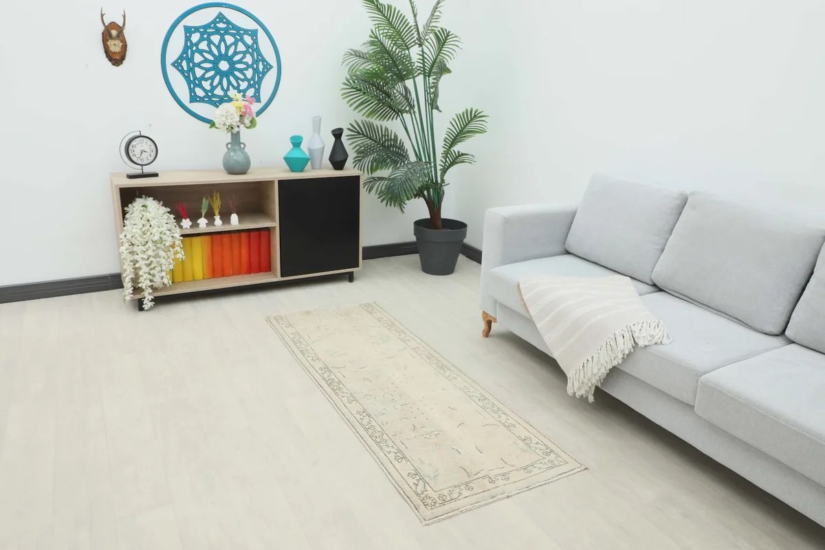 Beige vintage runner rug placed in a modern living space with a gray sofa and wooden cabinet.