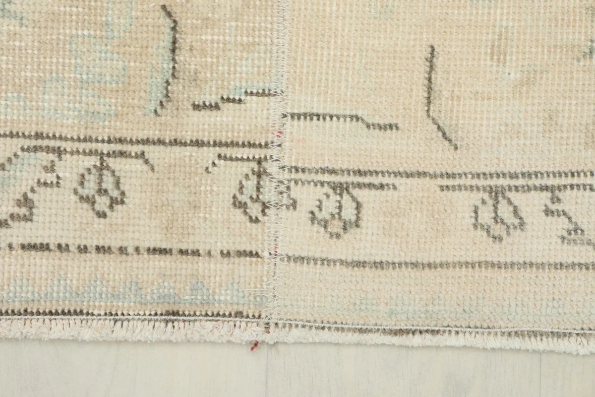 Detail of the rug's edge, showing the intricate border pattern in gray against the beige field.