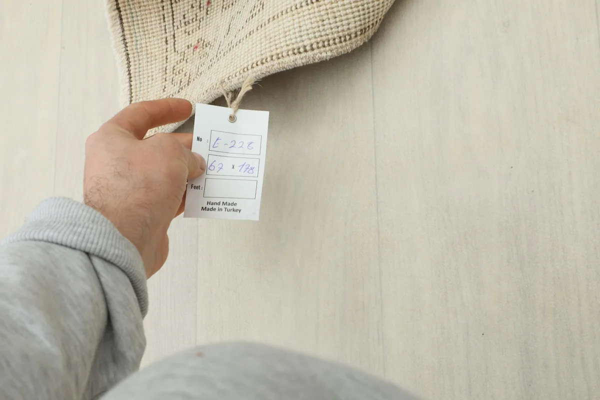 Hand holding the product tag, showing the size 2'2" x 5'10" (67 x 178 cm) and 'Made in Turkey' label.