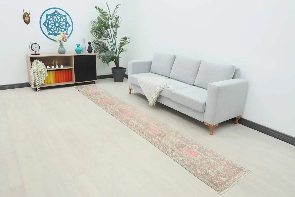 Long runner rug with rose and beige geometric patterns laid out in a living room setting next to a sofa