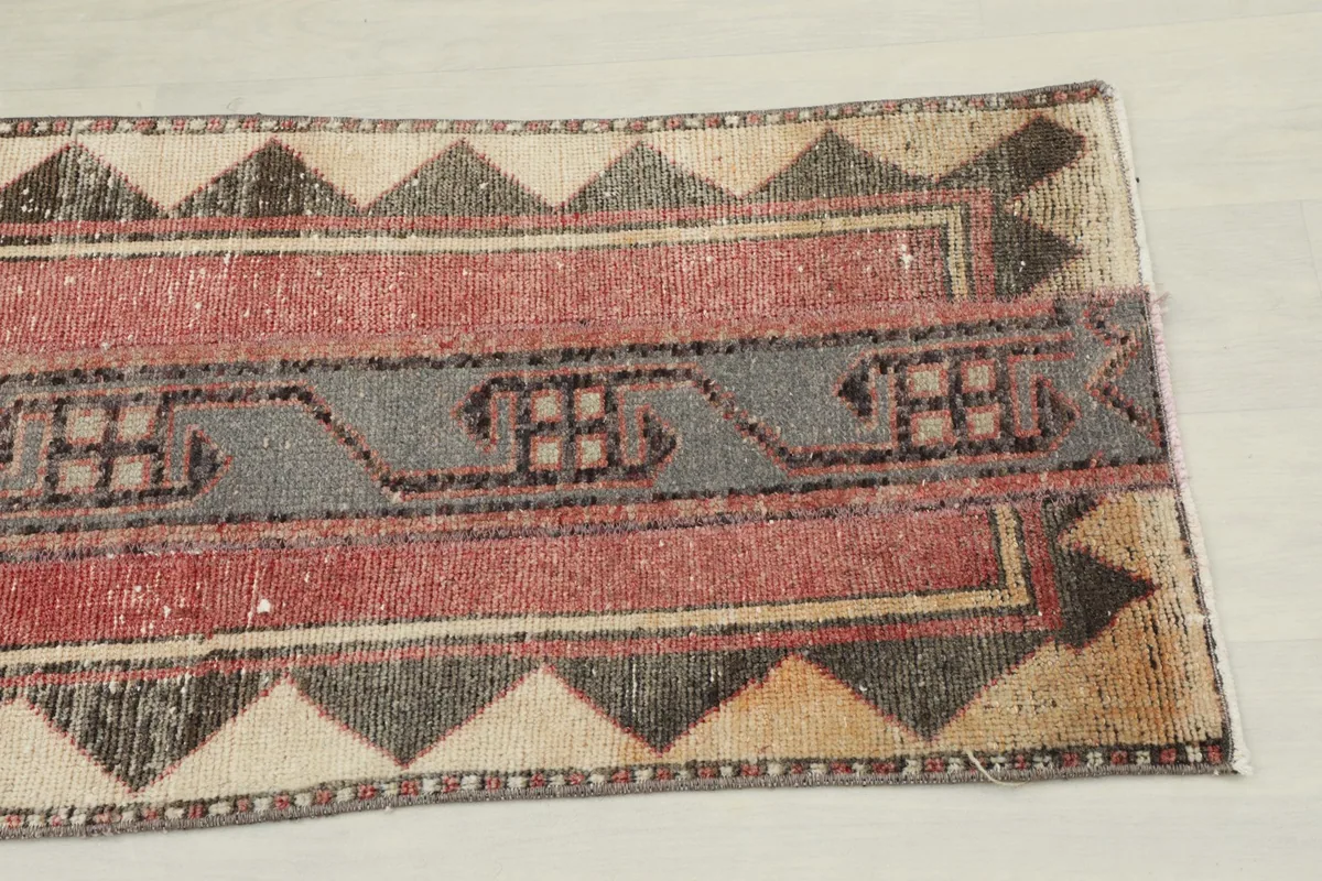 Close-up detail of one end of the runner rug, showing the tribal motifs in gray and rose, with beige and black triangles.