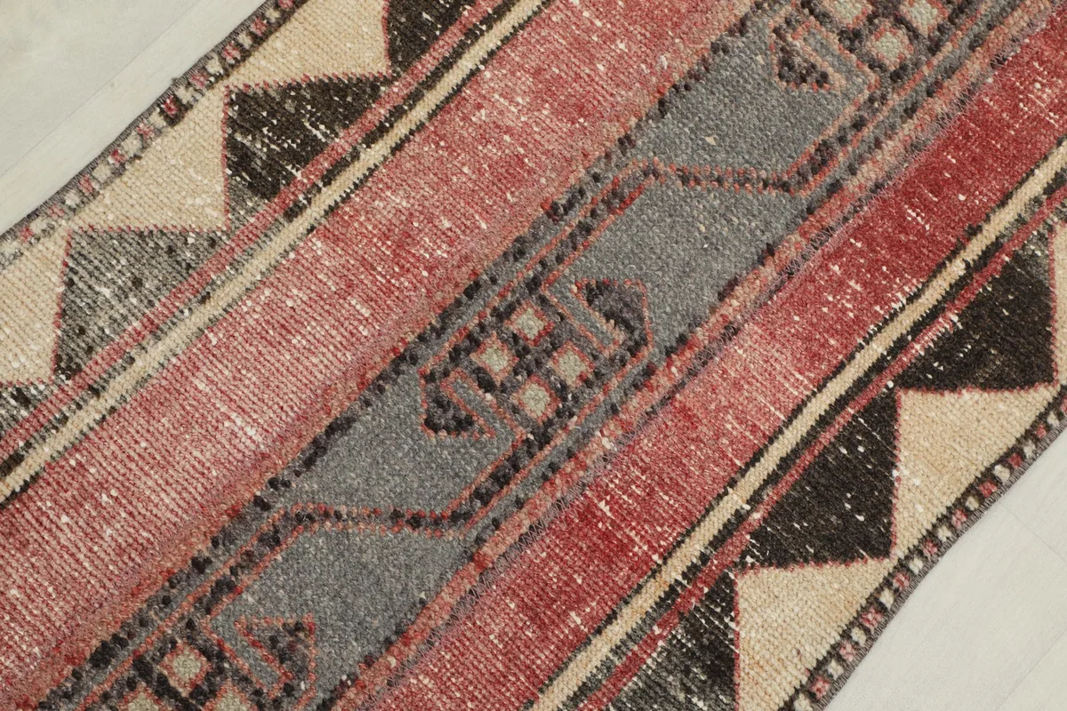 Diagonal close-up showing the texture and faded colors of the rose, gray, and beige geometric patterns on the runner.