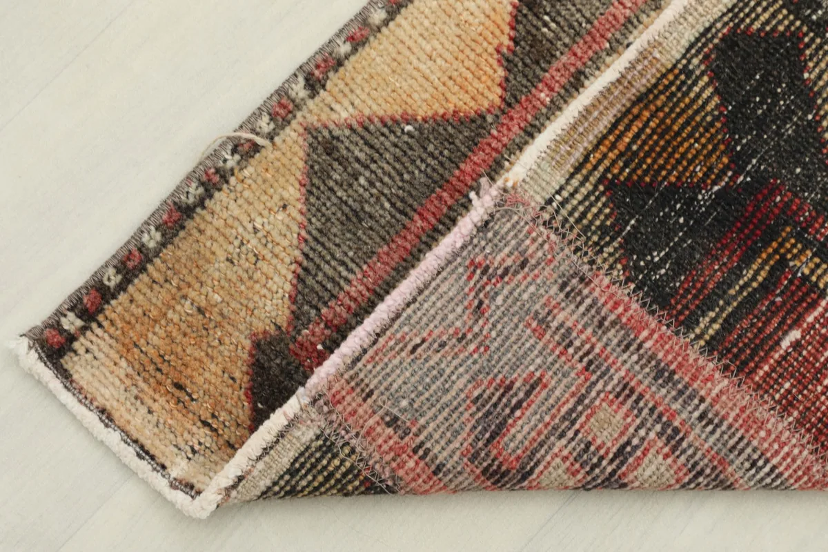 A section of the runner rug folded back, showing the wool pile and cotton foundation from the side.