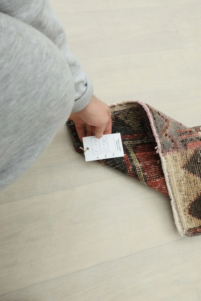 A hand holding a product tag near the rug, indicating its authenticity and details.