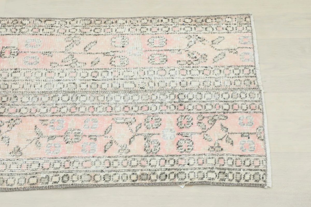 Close-up detail of the end of the pink and gray runner rug, showing floral and geometric motifs.