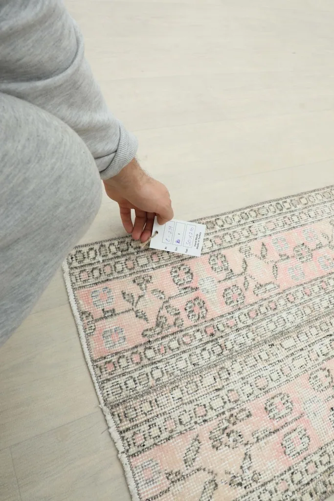 A hand holding a tag near the rug, indicating its professional cleaning and authenticity.