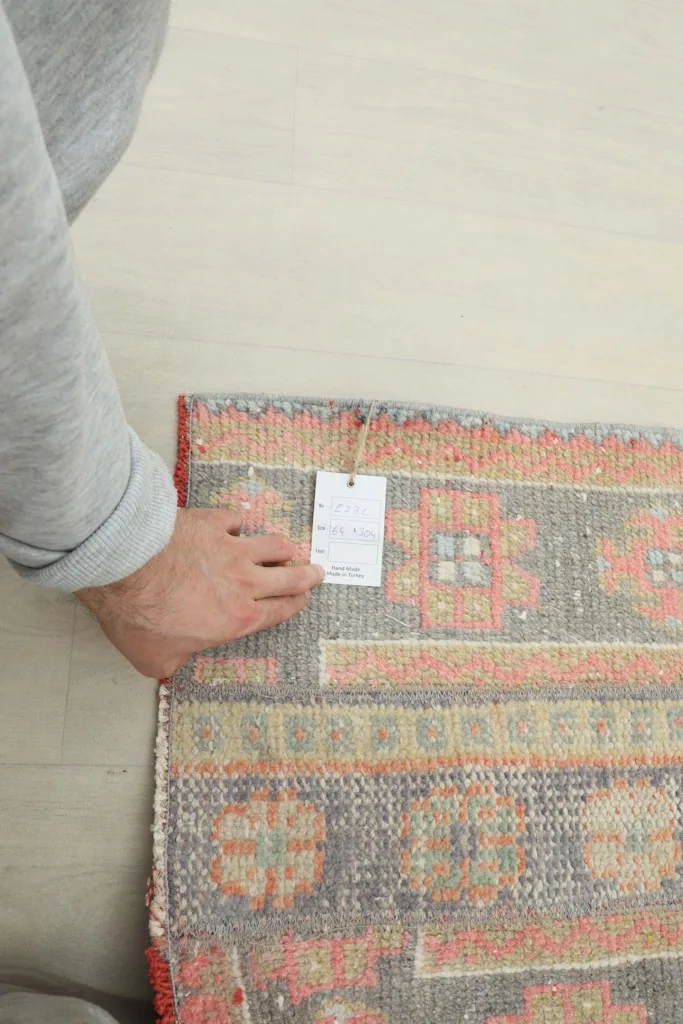 Hand holding a product tag on the rug, showing a small section of the pattern and fringe