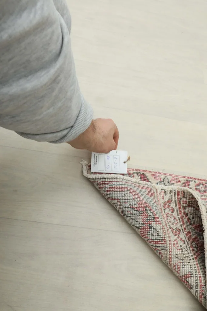 Hand holding a tag on the corner of the rug, indicating its authenticity and quality.
