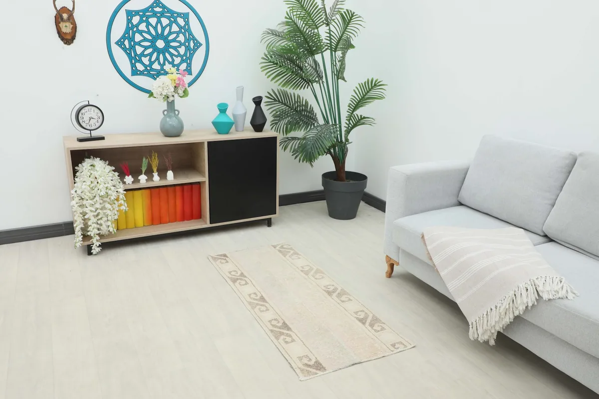 Beige vintage rug displayed in a living room setting with a light sofa and plant