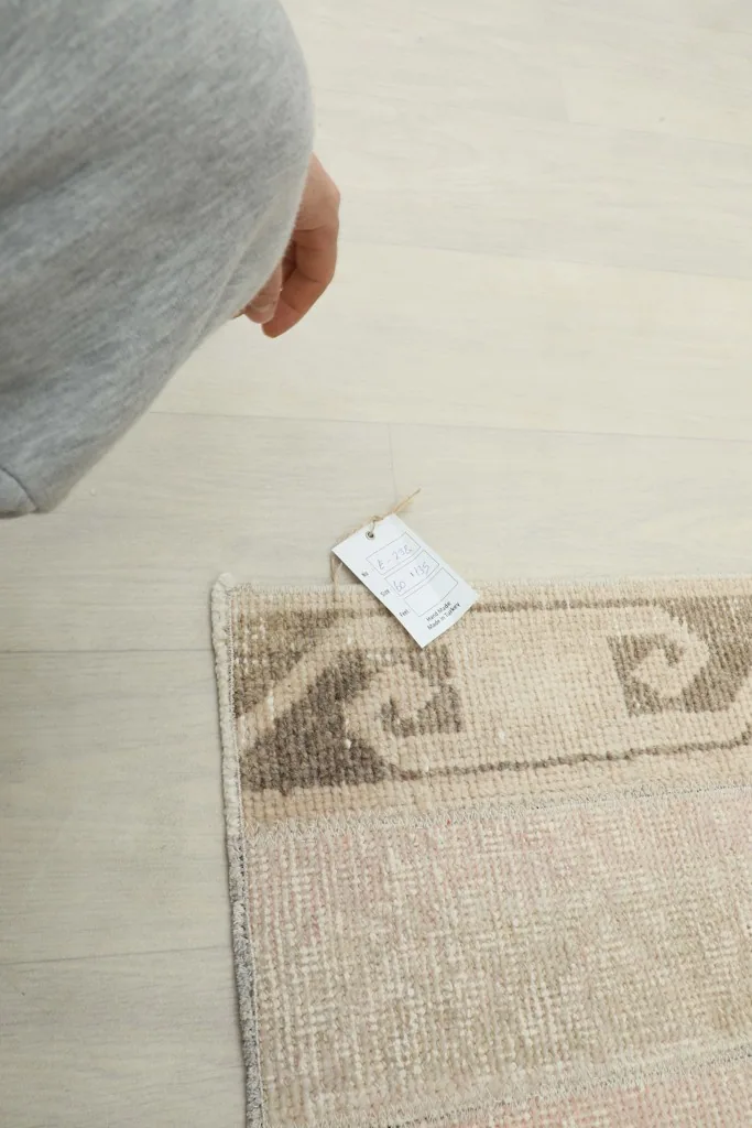 Hand holding a product tag near the corner of the beige vintage rug