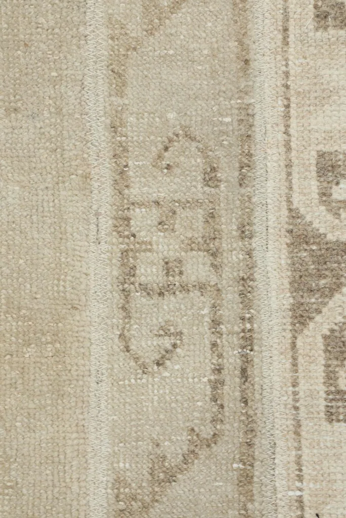 Extreme close-up of a brown tribal motif within the beige field, showing the hand-knotted wool pile.