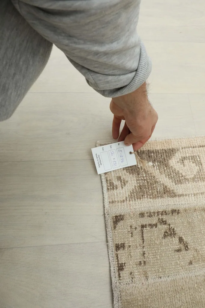 Hand holding a tag near the corner of the rug, indicating its size and other product information.