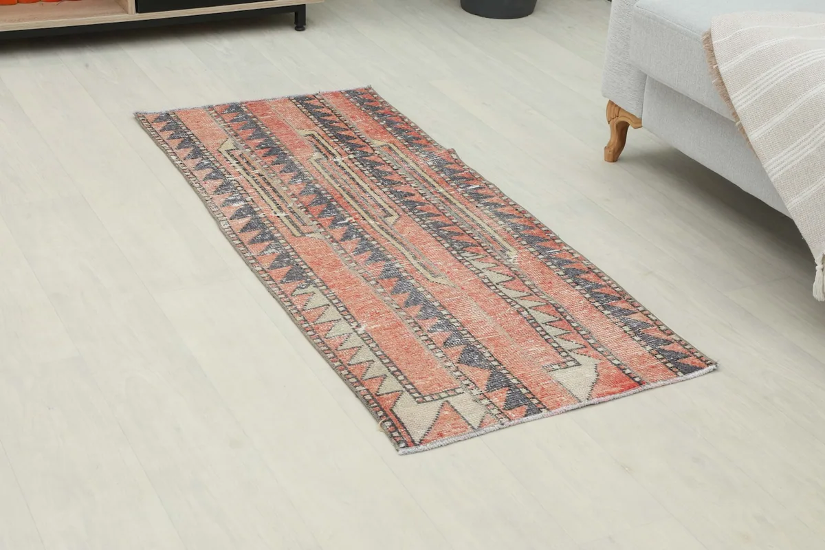 Angled view of the rug, highlighting its geometric patterns and muted red and gray colors.