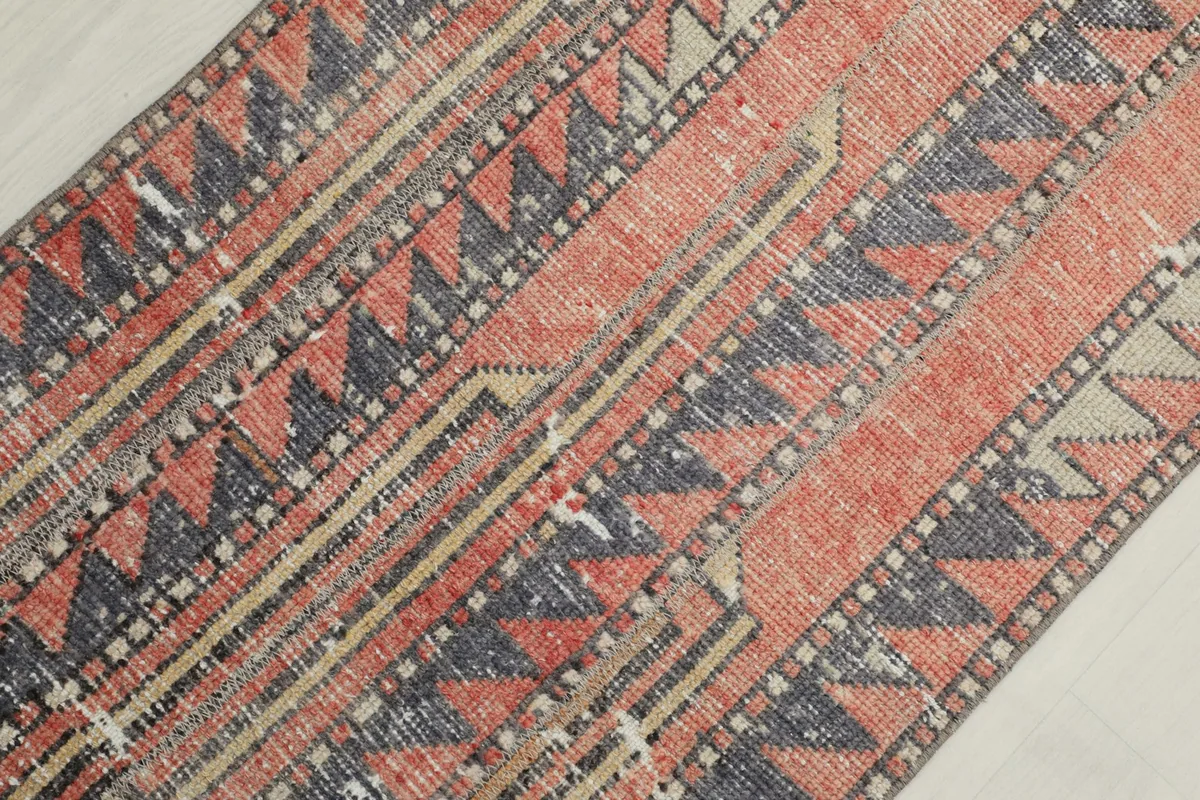 Close-up of the rug's central design, revealing the faded red pile and gray geometric motifs.