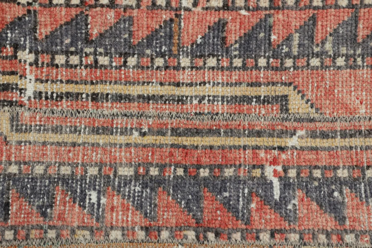 Extreme close-up of the hand-knotted wool pile, showing texture and color variation in red, gray, and beige.