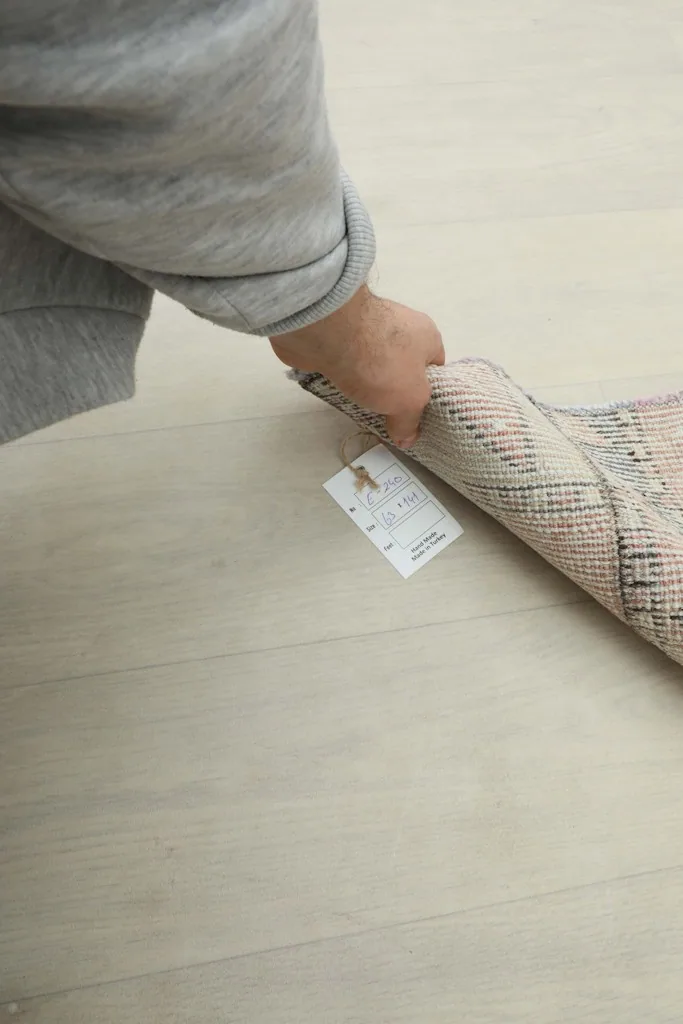 Hand holding a rolled section of the rug, showing its flexibility and the attached product tag.