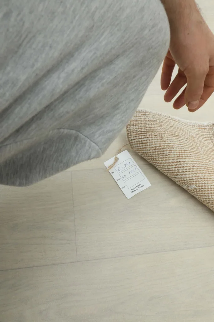 Hand pointing to the product tag, showing details and quality verification for the rug