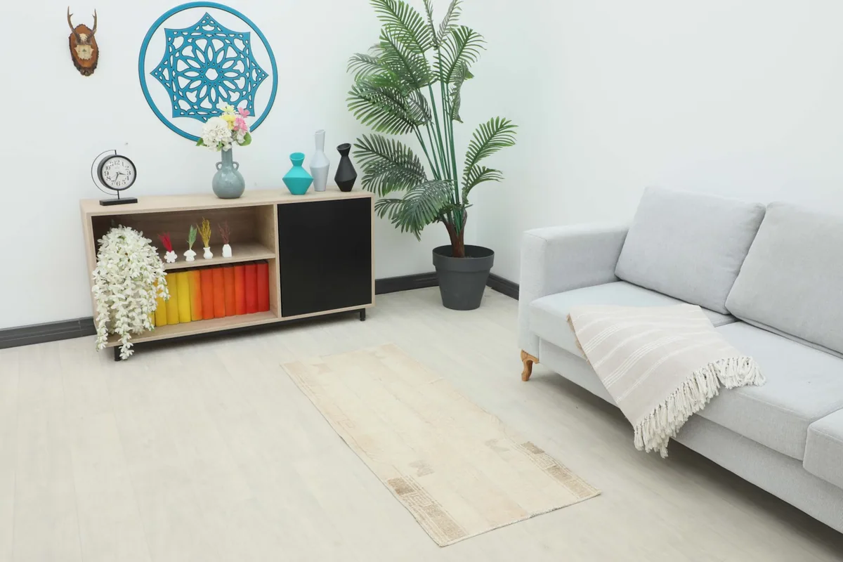 Vintage cream and beige rug placed in a living room setting with a light gray sofa and wooden cabinet.