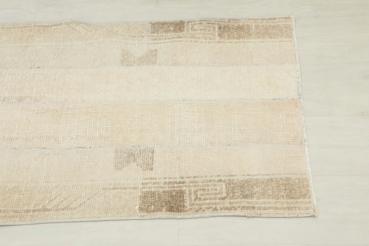 Close-up detail of the rug's end, showing the tan geometric border and faded cream field.