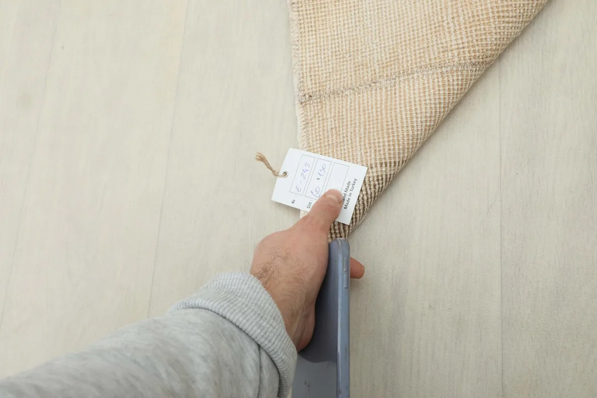 Hand holding the product tag on the back of the vintage hand-knotted rug.