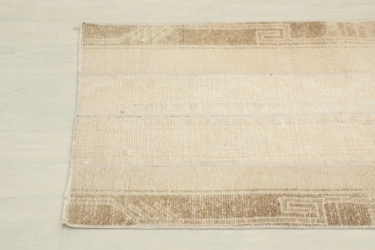 Close-up of the other end of the runner rug, showing the tan border design and subtle field patterns.