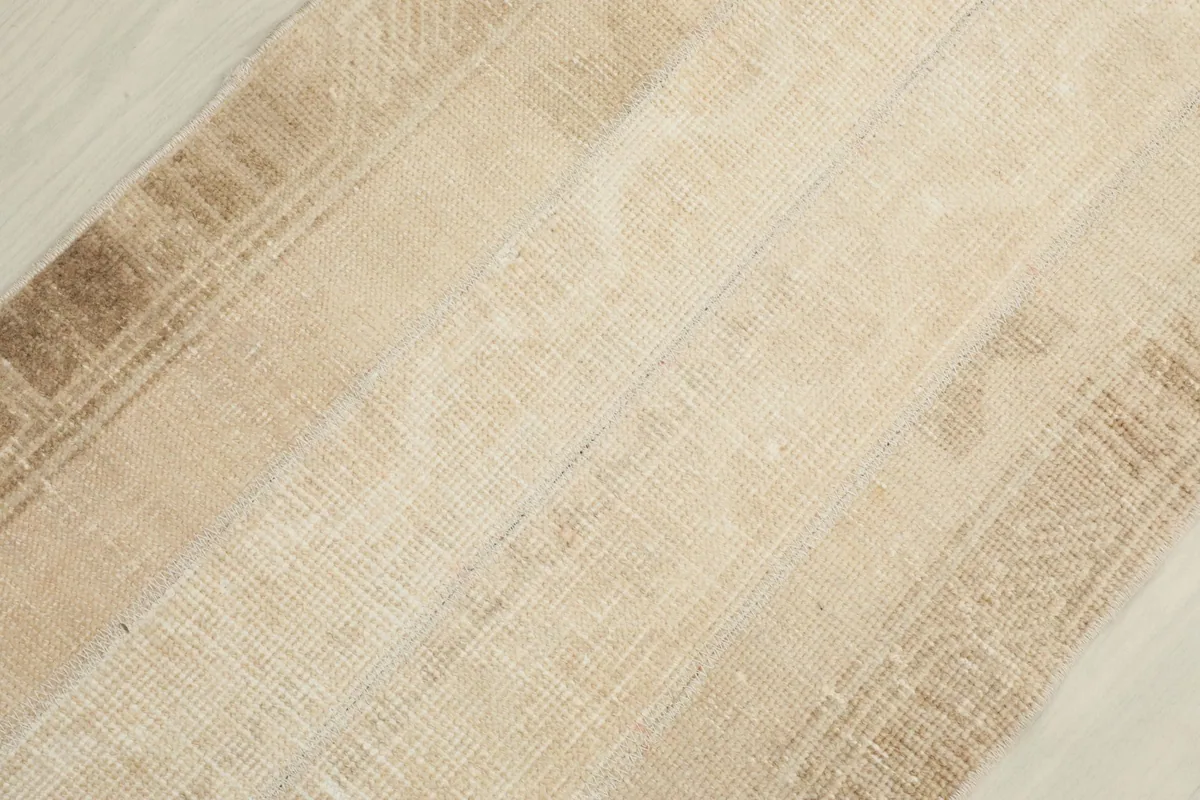 Diagonal view of the rug's low pile, revealing the texture and subtle color variations in the ivory and tan.
