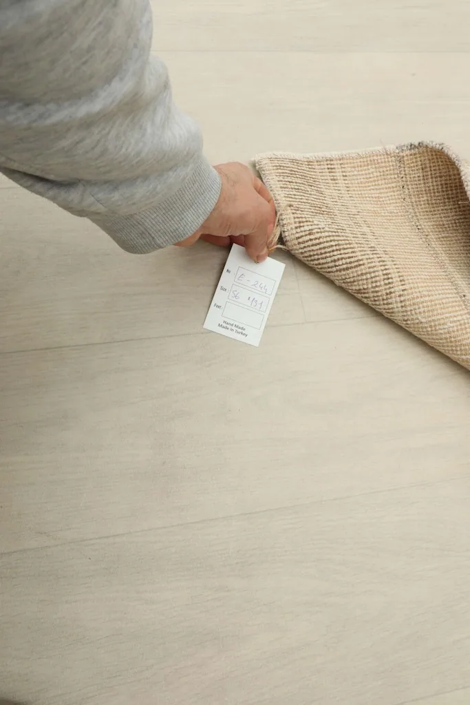 Hand holding a product tag near the folded rug, indicating its professional cleaning and quality.