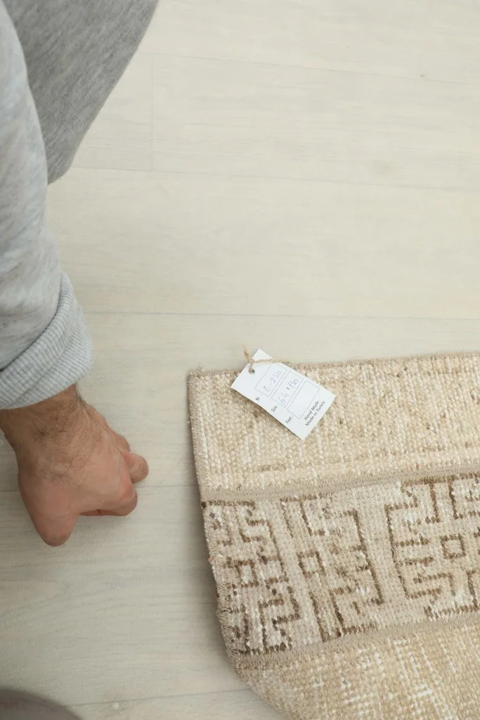 Hand next to the rug's edge, showing the size and scale with a small tag attached.