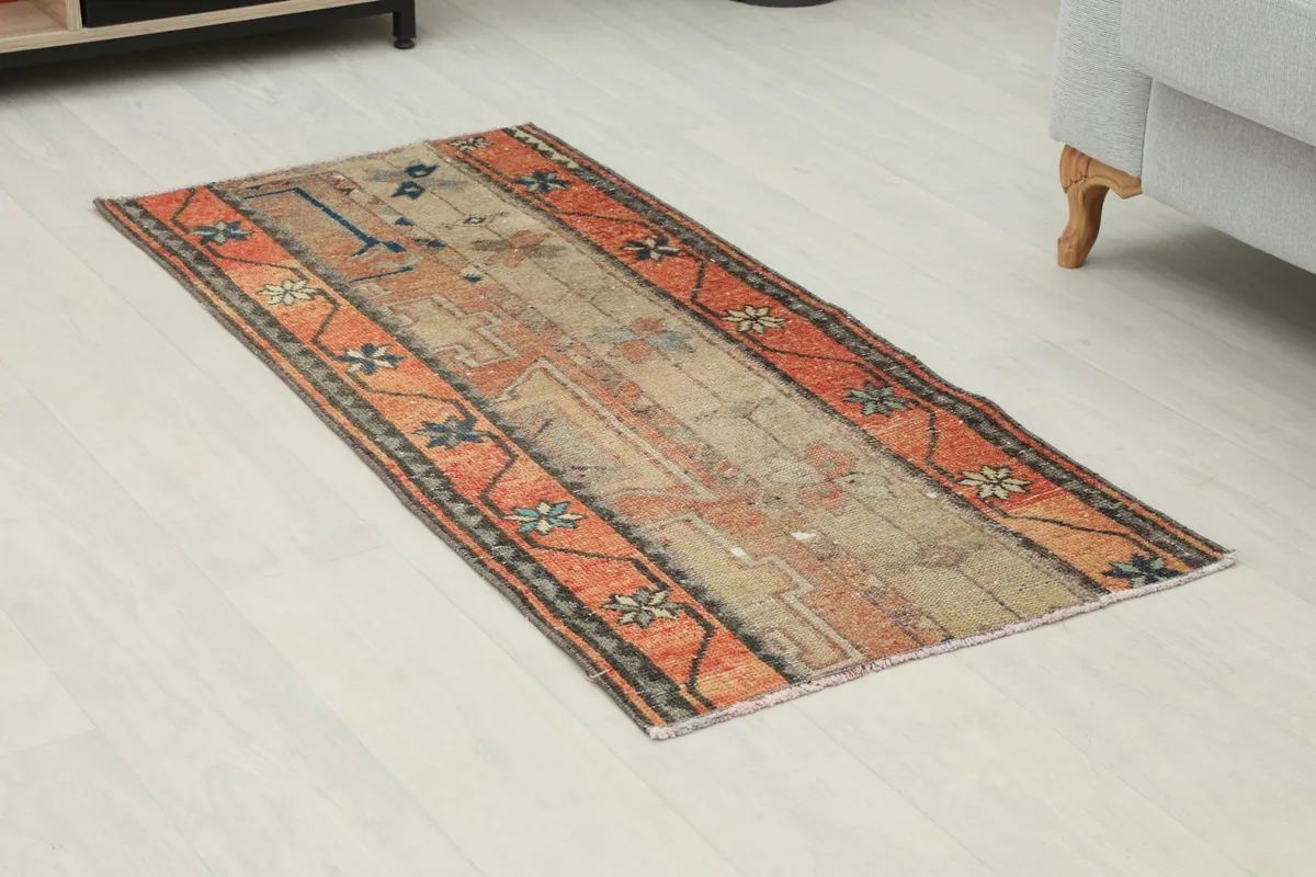 Angled view of the vintage orange and beige rug on a light floor, showing its full length.