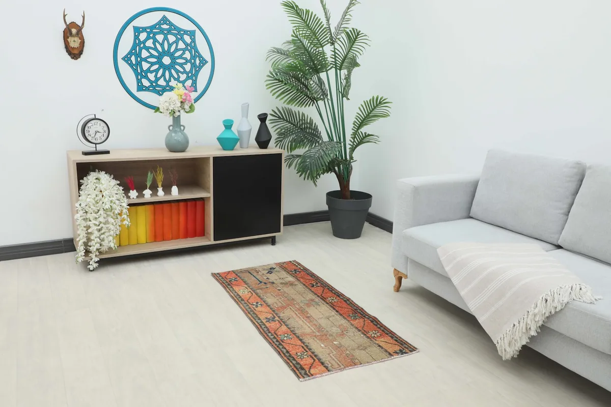 Vintage orange and beige rug displayed in a modern room setting next to a sofa and cabinet.