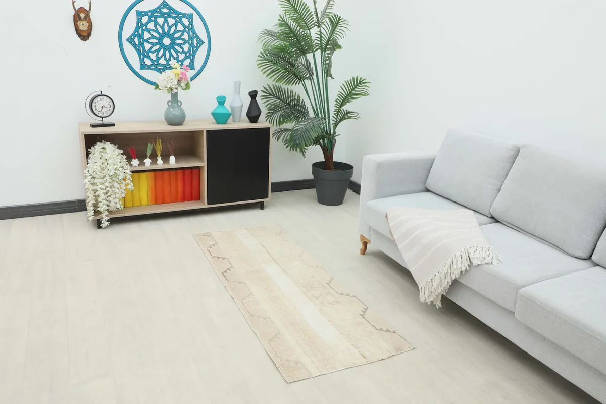 Cream and beige runner rug displayed in a living room setting with a light gray sofa and wooden cabinet.