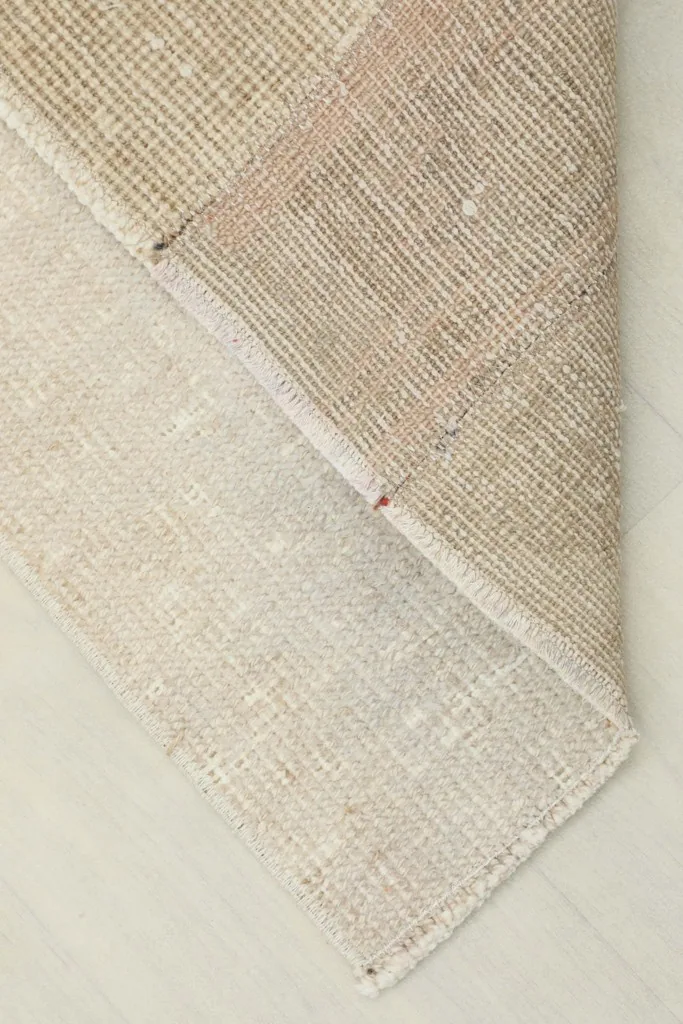 Corner view of the rug folded back, revealing the cotton foundation and reverse side of the weave