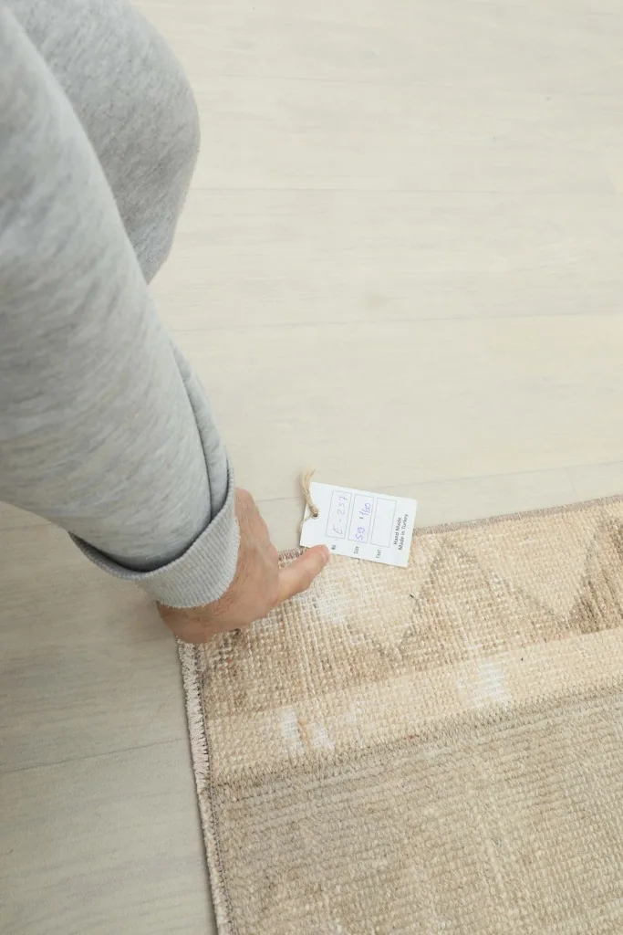 A hand holding the RugsKilim tag next to the vintage Anatolian runner rug, showing scale.