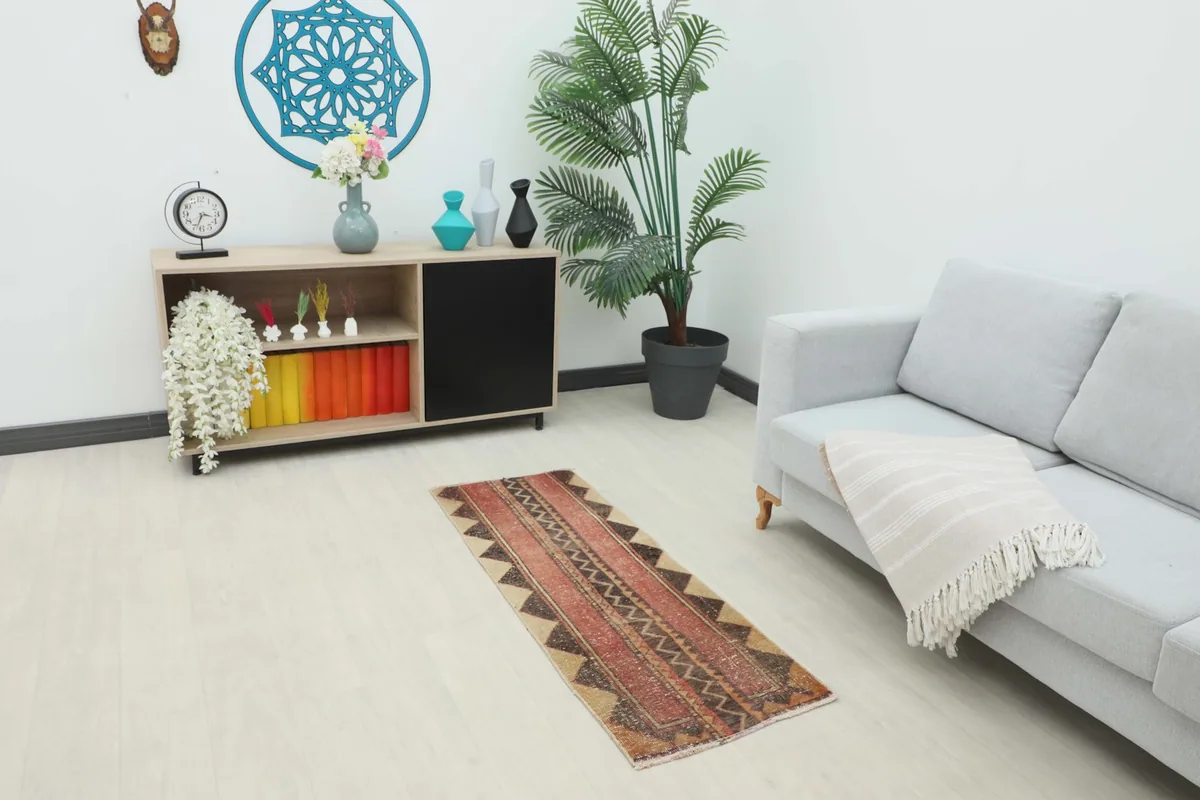 The red and tan runner rug placed in a modern living space with a sofa and console.