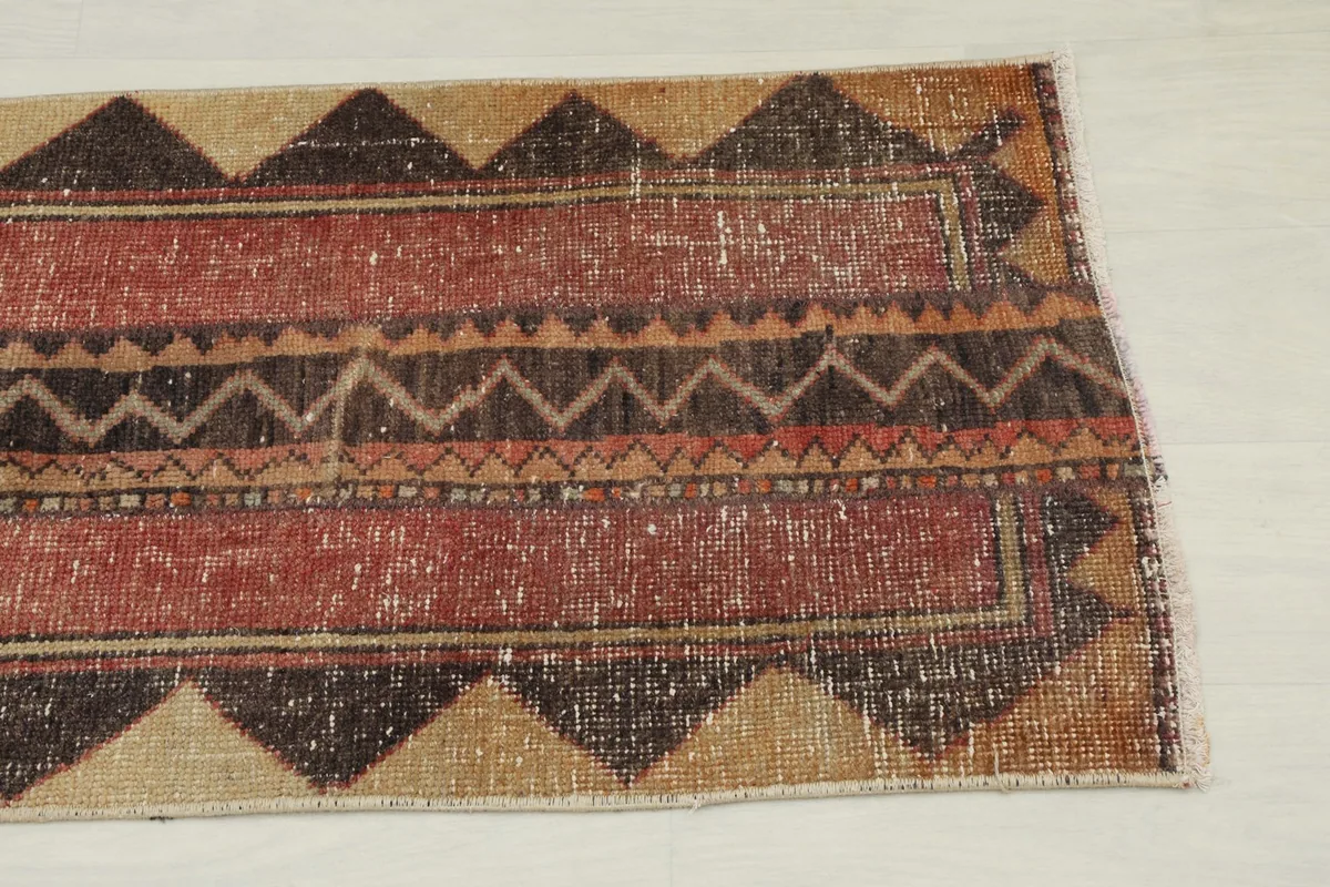 Close-up detail of the rug's end, showing the red field, tan border, and brown tribal motifs.