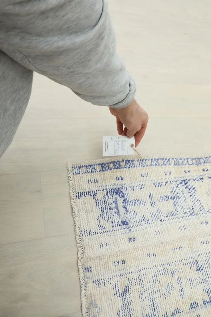 Hand holding a product tag near the corner of the blue and ivory vintage runner