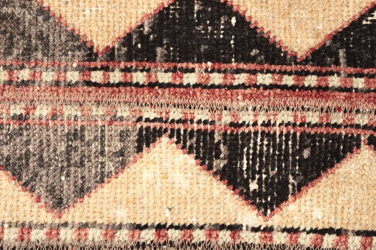 Detailed shot of the rug's central design, featuring black, gray, and rust diamond motifs and low pile.