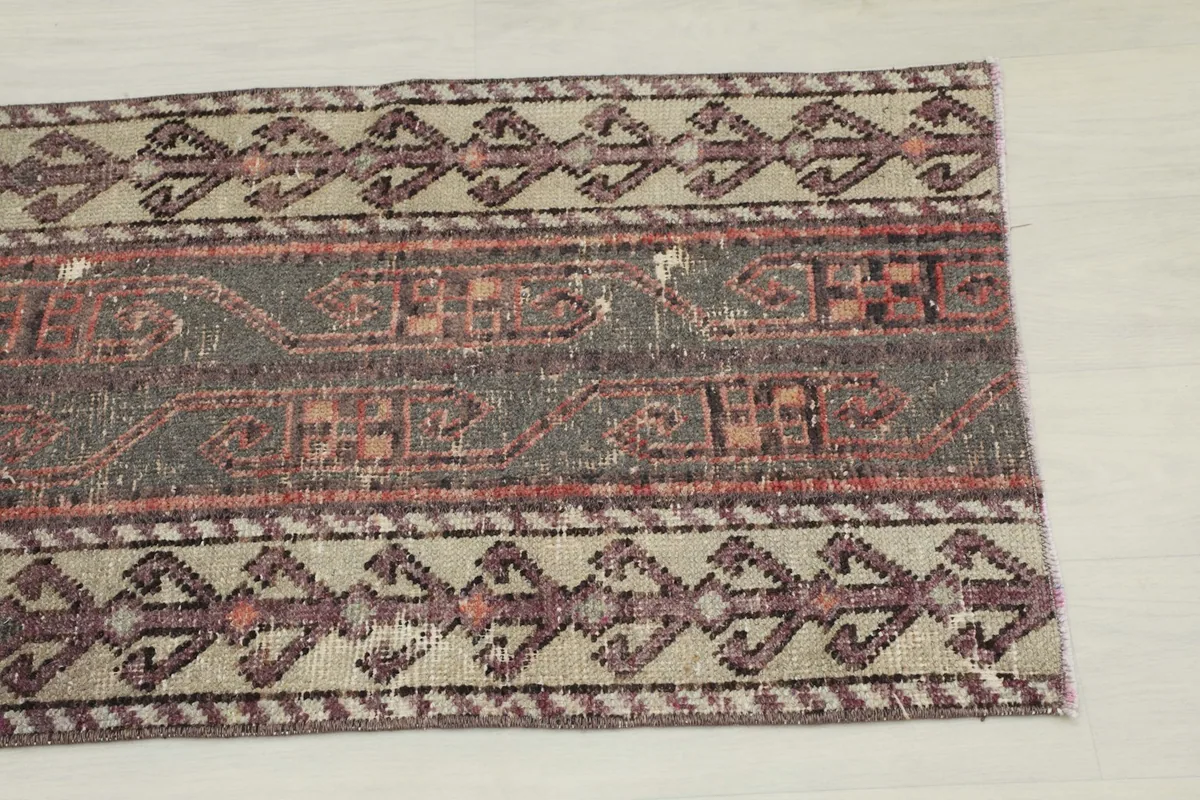 Close-up of one end of the rug, showing the faded charcoal field and beige border with rose geometric motifs.