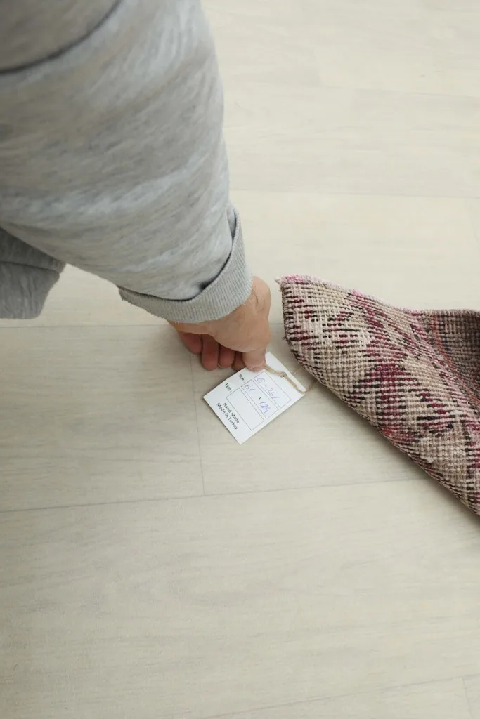 A hand holding a product tag next to the folded rug, indicating its unique identification.