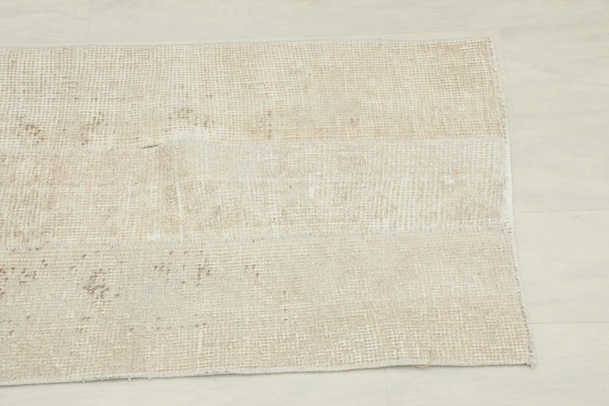 Close-up of one end of the tan runner rug, showing the texture and faded geometric design.