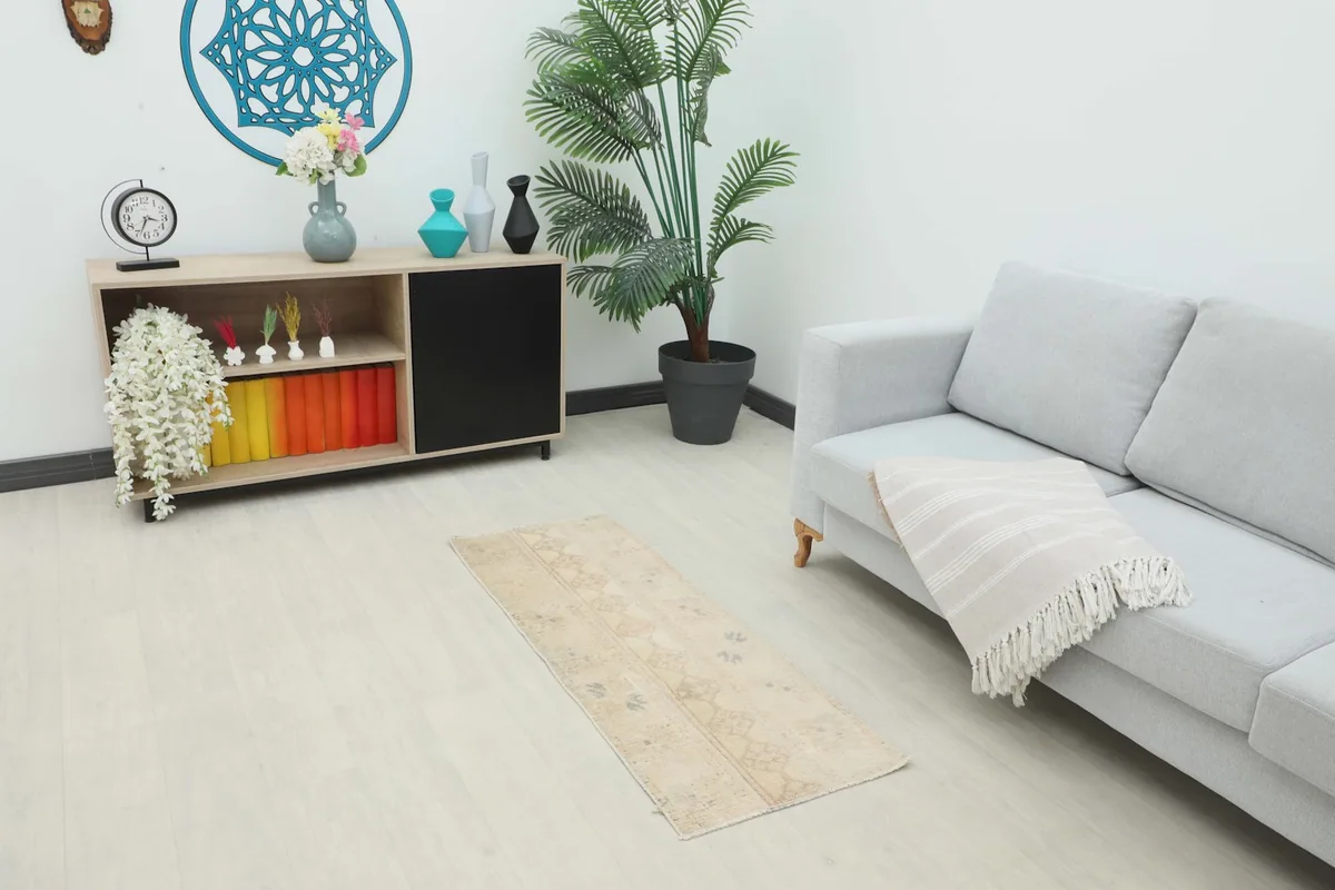 Vintage beige runner placed in a living room setting, showing its scale next to a sofa.