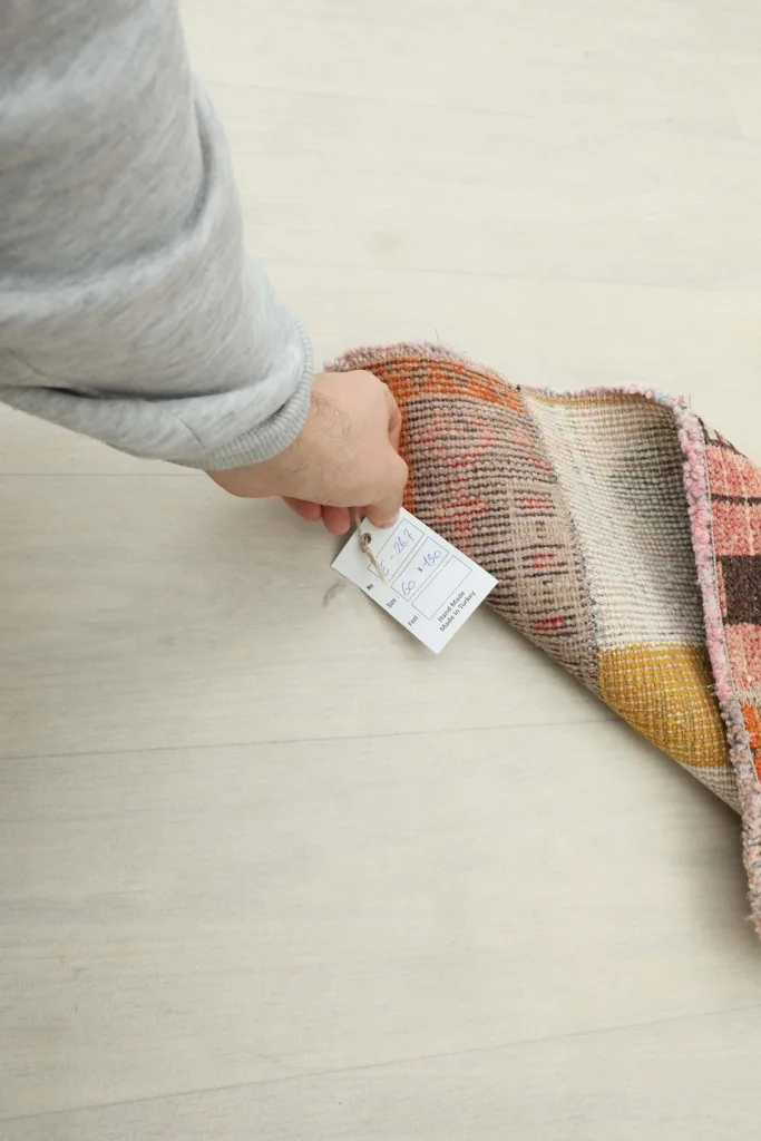 Hand holding a tag, with the rug's back visible, showing the cotton foundation.