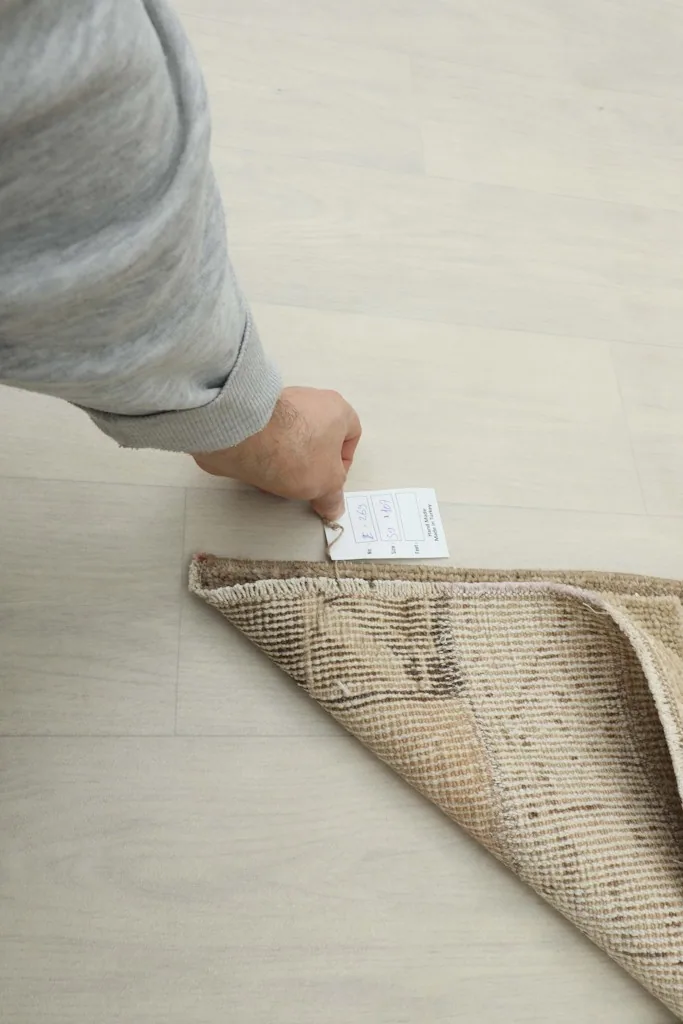 A hand pointing to the back of the rug, illustrating its authentic vintage tag.