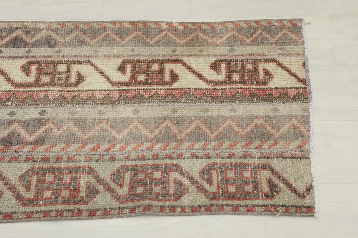 Close-up of one end of the rug, showing beige, brown, and rose tribal geometric patterns.