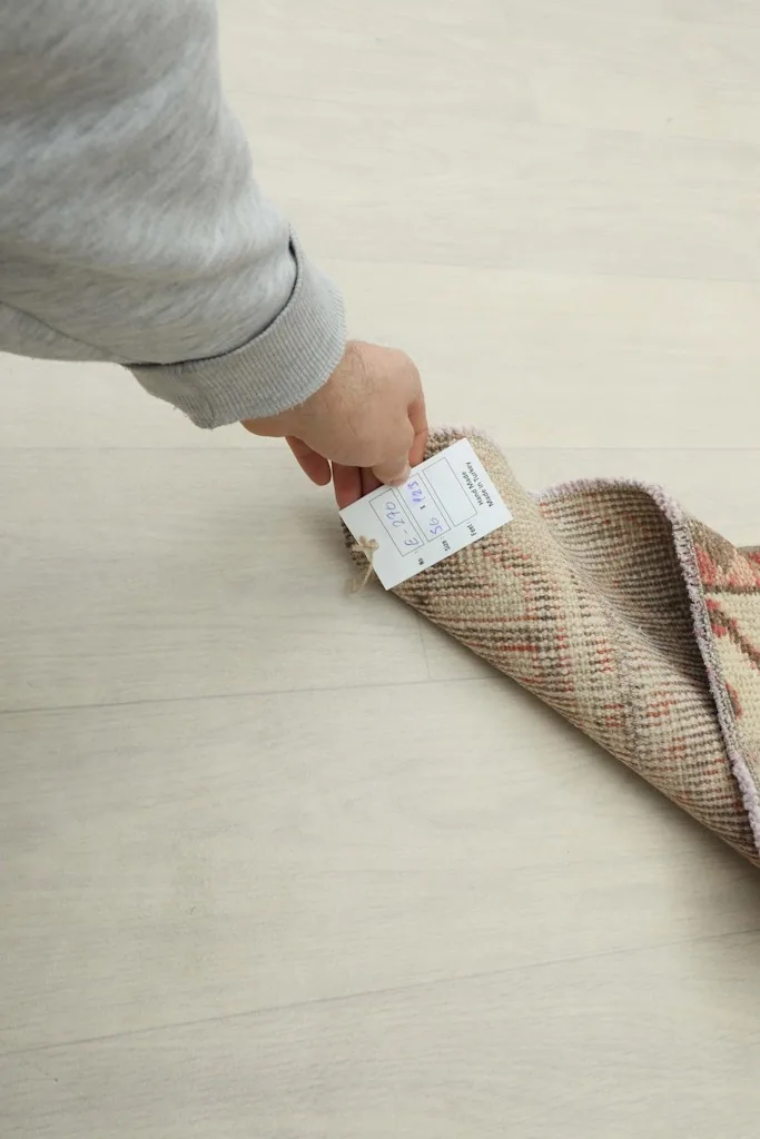 A hand holding a product tag against the folded rug, indicating its quality and origin.